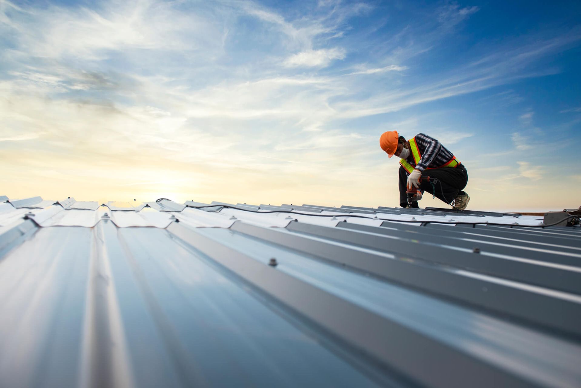 Arbeiter in Warnweste und Helm bei der Montage eines Metalldachs bei Sonnenuntergang.