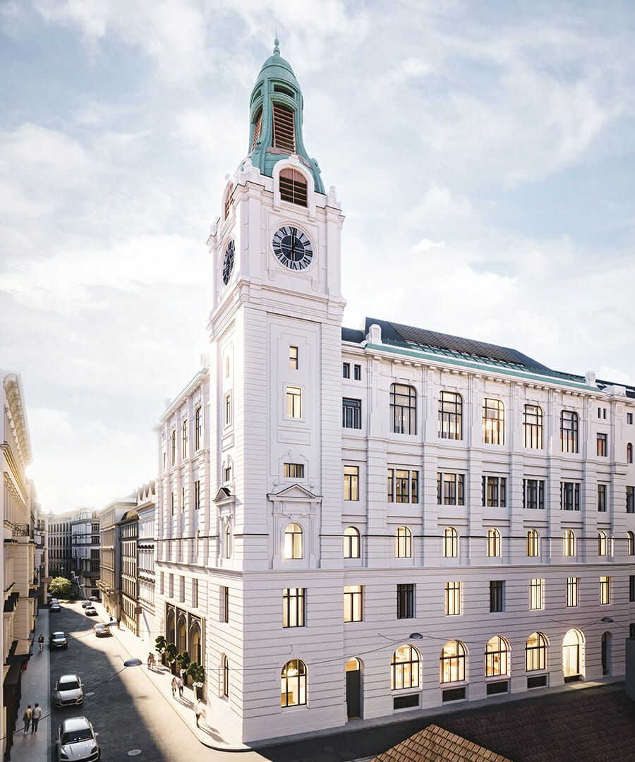Weißes historisches Gebäude mit Uhrenturm, in Sonnenlicht getaucht, vor einem blauen Himmel.